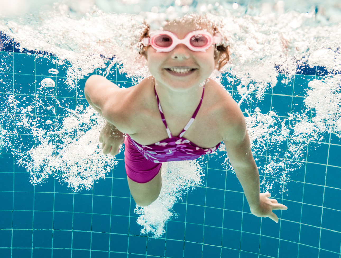 Girl smiles, swimming under water in the pool Albuquerque Moms Blog